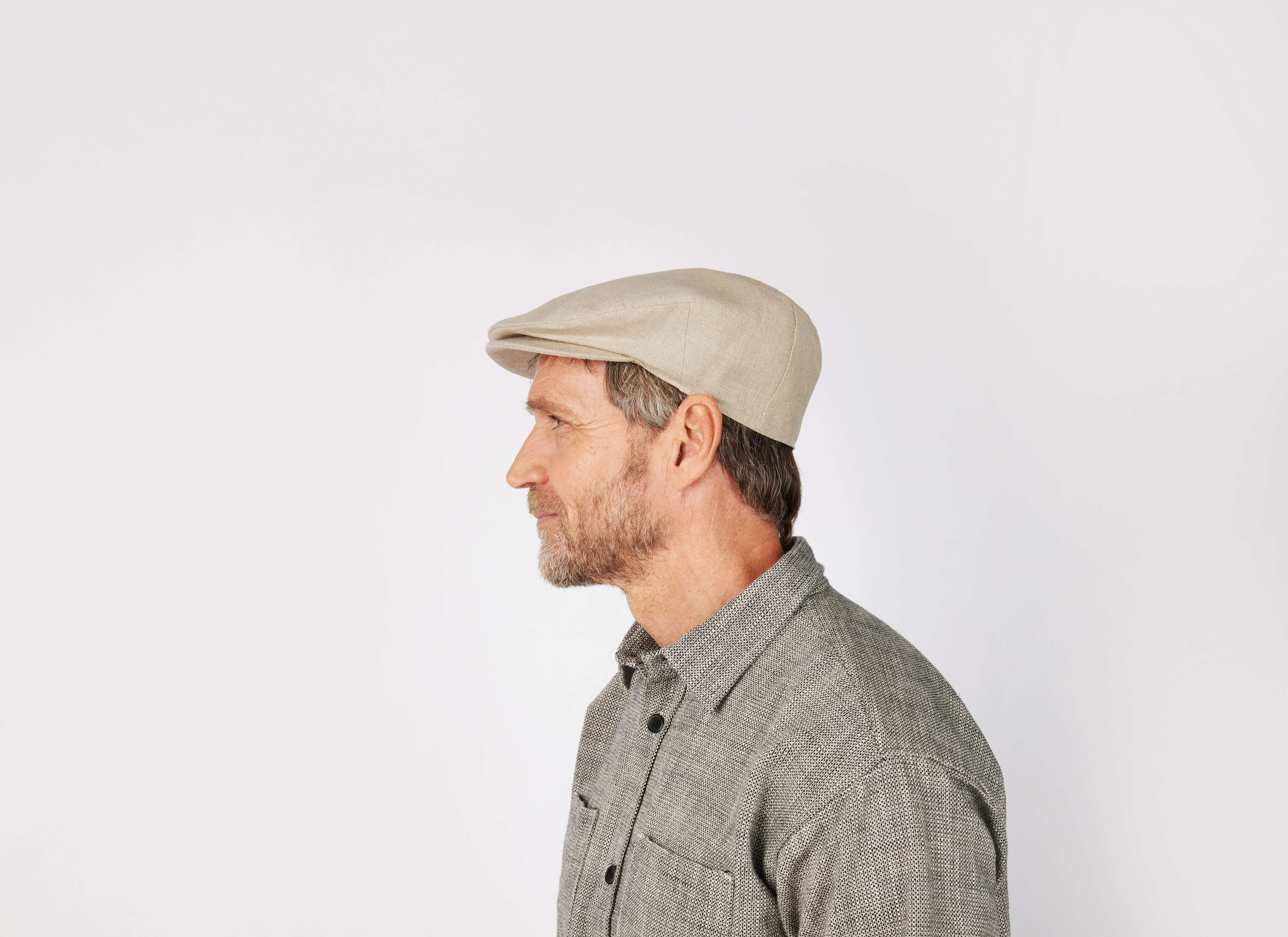 A man with a short beard wears the Vintage Cap Linen by Hanna Hats and a gray button-up shirt, shown in profile against a plain white background.