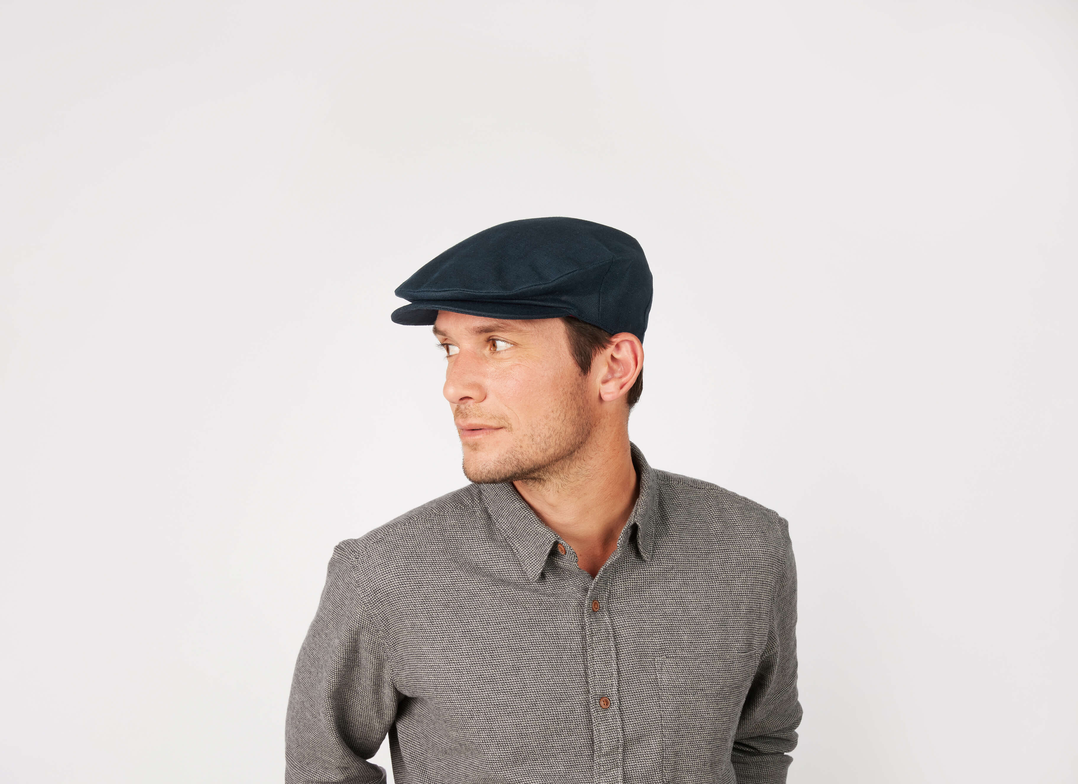 A man wearing the Vintage Cap Linen by Hanna Hats and a gray button-up shirt looks to his left against a plain white background.