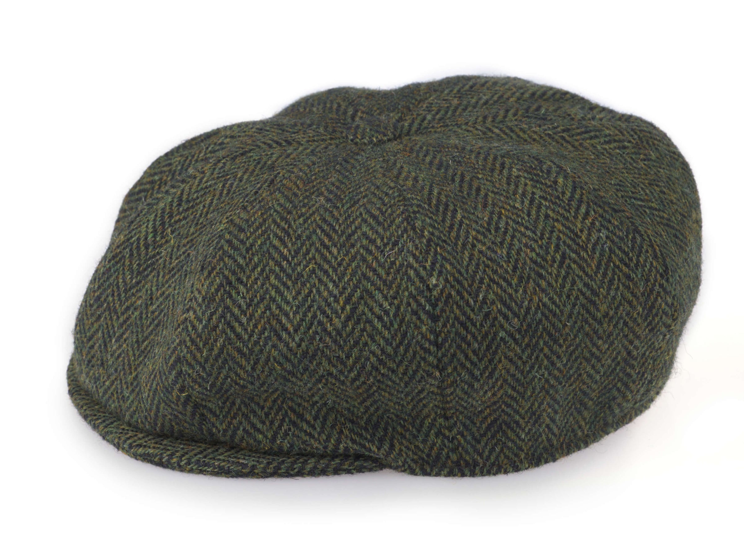 The Connery Cap Tweed by Hanna Hats is a green herringbone flat cap with a rounded crown and short, stiff brim, offering timeless style inspired by Sean Connery. Shown on a white background.