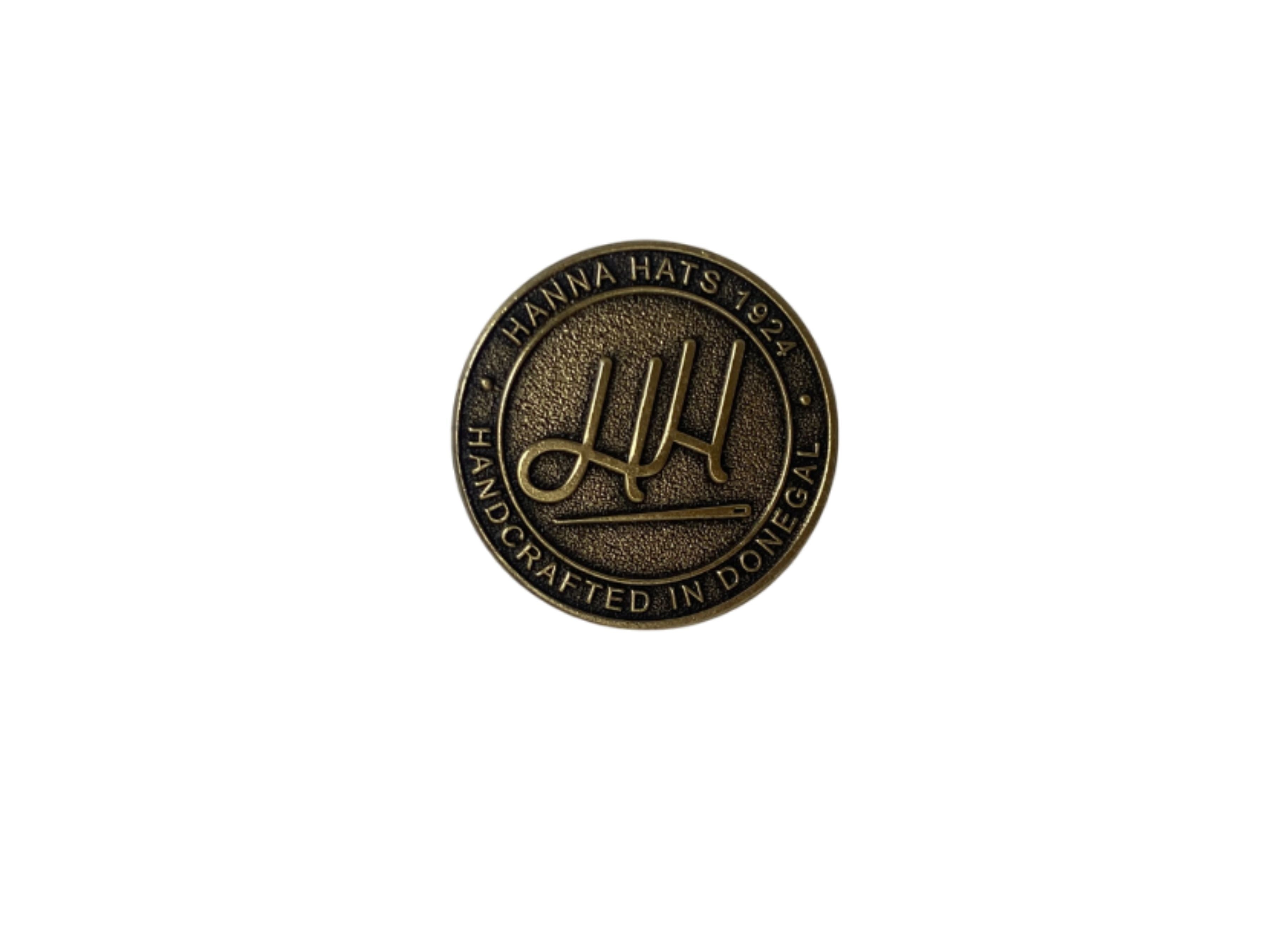 The Hanna Hats Pin by Hanna Hats of Donegal Ltd is a round bronze pin with a brushed gold finish, featuring “HANNA HATS 1924 HANDCRAFTED IN DONEGAL” around a stylized “HH” logo for a true heritage look.