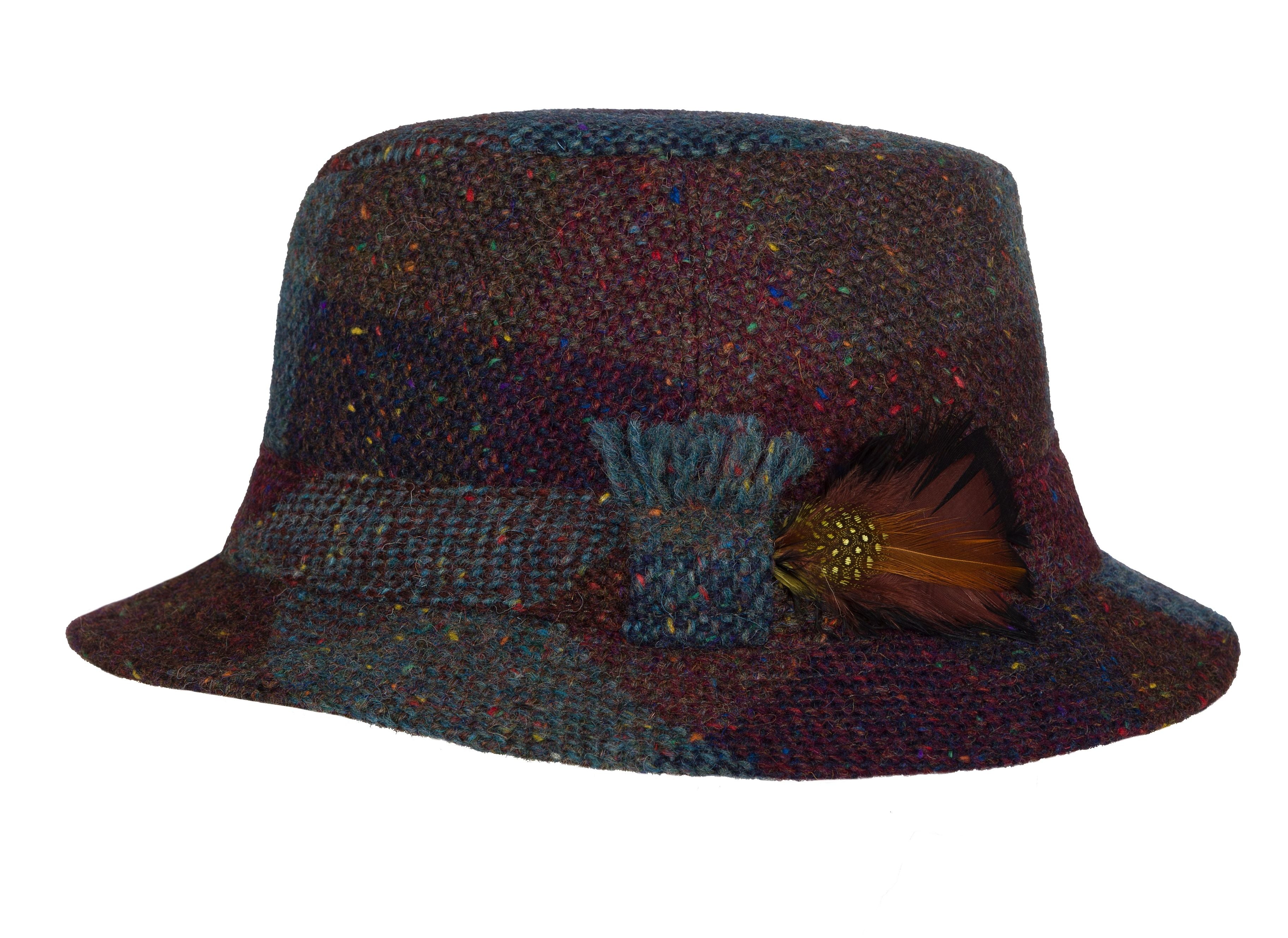 The Walking Hat Tweed by Hanna Hats is a multicolored Irish tweed bucket hat with a wide brim, decorative band, fabric knot, and brown feather accent—classic style inspired by traditional Donegal walking hats.