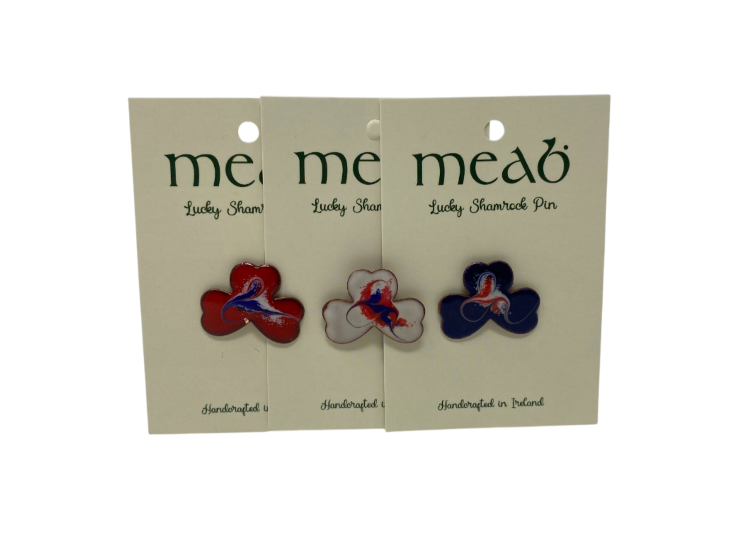 Three “Meab Enamels” Lucky Shamrock Pendants by Hanna Hats of Donegal Ltd, each with a red, blue, or white bird design at the center of a shamrock. These pendants highlight handmade Irish artistry.